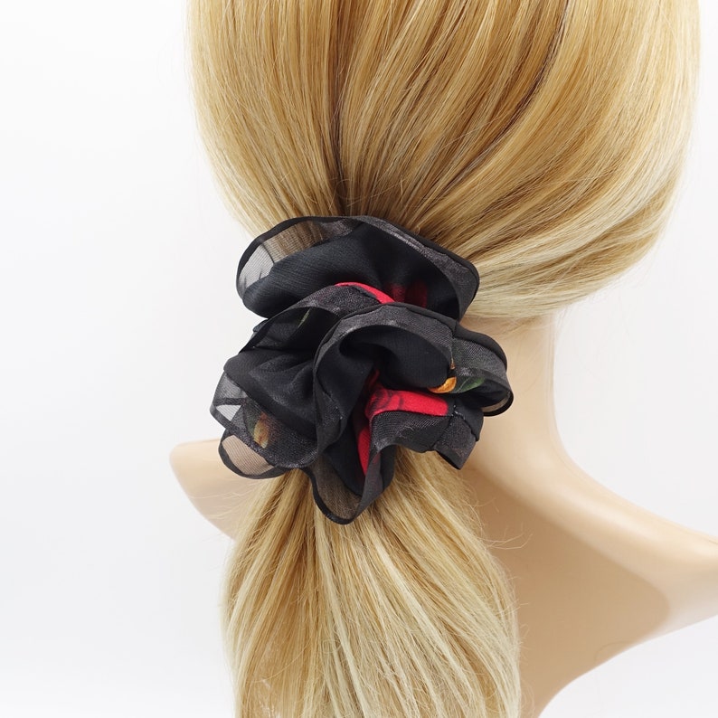 May include: A black and red floral hair scrunchie made of soft fabric. The scrunchie is tied around a ponytail.
