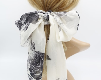 May include: White chiffon hair tie with a black floral print. The bow is tied in a large, loose knot.
