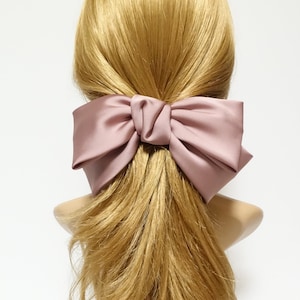 Op de afbeelding: Een grote, stoffige roze satijnen strik haarclip. De strik is in een grote, losse knoop geknoopt en is vastgemaakt met een clip.