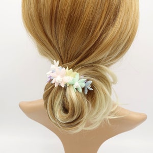 May include: A pastel floral hair clip with pink, yellow, blue, and white flowers. The clip is worn in a woman's hair.