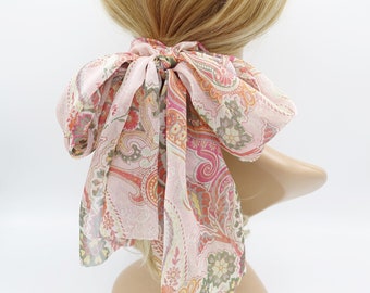 May include: A pink and green paisley patterned hair scarf tied in a bow.