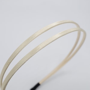 May include: A simple, double-layered headband made of a soft, off-white fabric. The headband is flexible and has a black elastic band at the back.