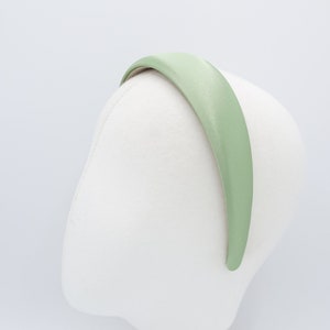 May include: A light green satin headband is displayed on a white mannequin head. The headband is a solid color and has a smooth, shiny texture. The headband is curved to fit the head.