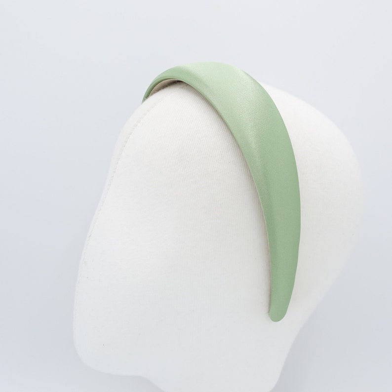 May include: A light green satin headband is displayed on a white mannequin head. The headband is a solid color and has a smooth, shiny texture. The headband is curved to fit the head.