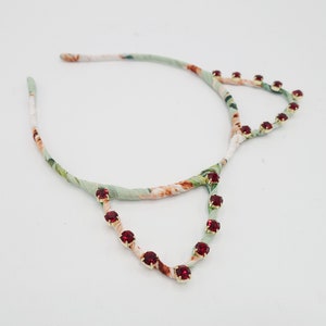 May include: A green and white floral headband with red rhinestone accents in the shape of cat ears.
