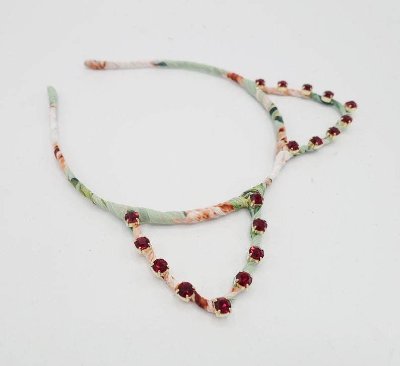 May include: A green and white floral headband with red rhinestone accents in the shape of cat ears.
