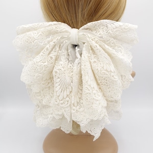 May include: A large white lace bow hair tie. The bow is made of delicate white lace and is tied in a large, full bow.