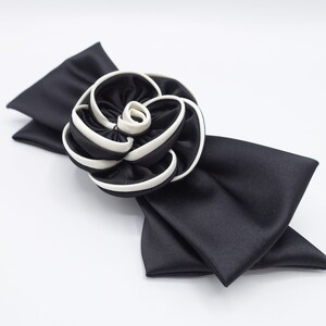 May include: A black satin bow with a white and black fabric rose.