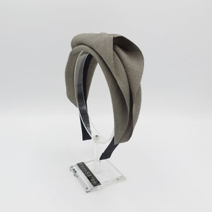 May include: A gray fabric headband with a knotted design. The headband is on a clear display stand.