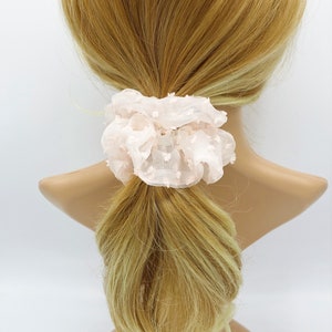 May include: A light pink hair scrunchie with white polka dots. The scrunchie is made of a soft, stretchy fabric and is perfect for holding a ponytail or braid.