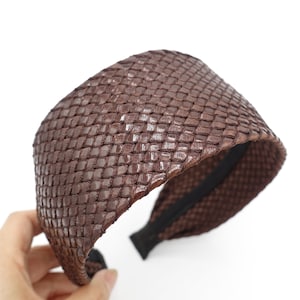 May include: A brown woven headband with a wide, flat band and a stretchy elastic back.