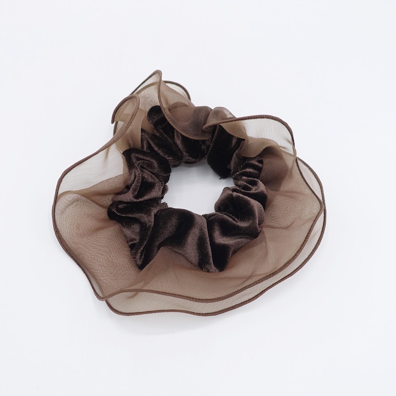 May include: A brown scrunchie with a velvet center and a sheer, ruffled outer layer. The hair accessory is a rich, dark brown color, perfect for adding a touch of elegance to any hairstyle. The scrunchie is designed to hold hair securely.