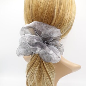 May include: A gray, sheer, large scrunchie made of fabric. The scrunchie is tied around a ponytail.