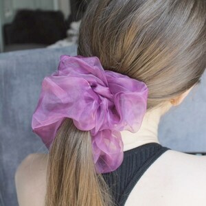 May include: A purple scrunchie made of sheer fabric, tied in a ponytail on a person's head.