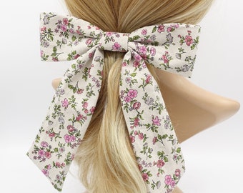 May include: A large beige bow with a pink and green floral print. The bow is tied around a ponytail.