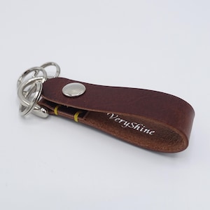 May include: A brown leather key chain with a silver key ring and a silver button. The keychain has the text "VeryShine" embossed on it.