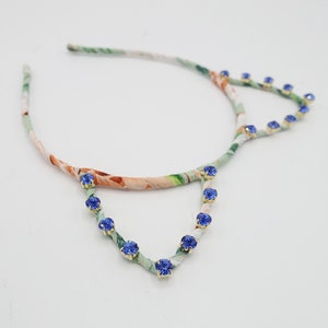 May include: A floral patterned headband with blue rhinestone accents. The headband is made of fabric and has a wire frame.