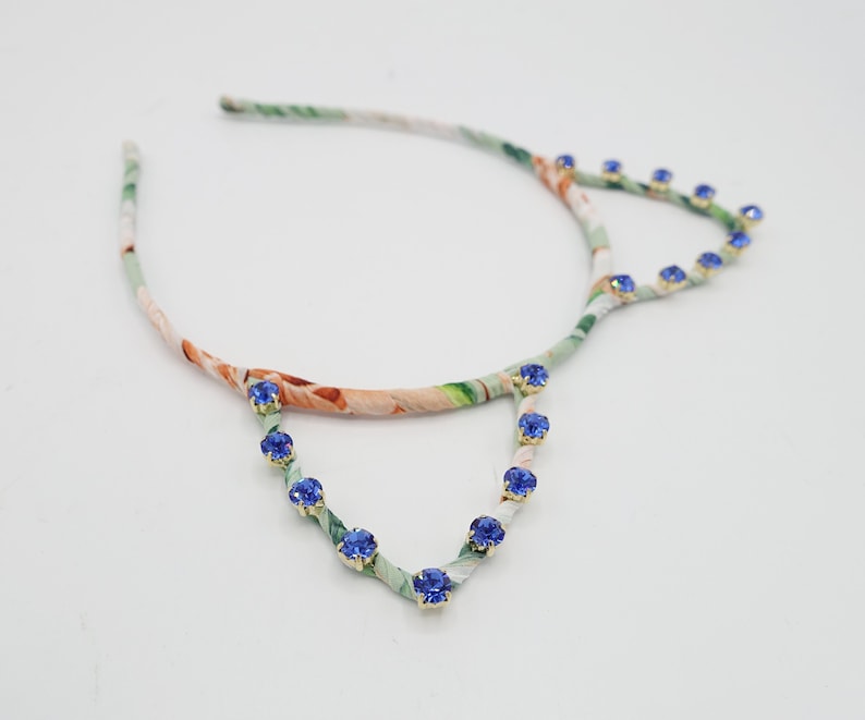 May include: A floral patterned headband with blue rhinestone accents. The headband is made of fabric and has a wire frame.