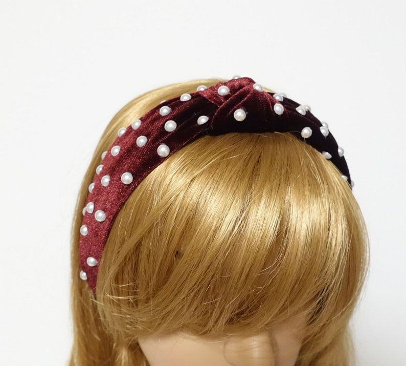 May include: A burgundy velvet headband with a knotted design and white pearl embellishments.
