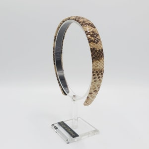 May include: A brown and beige snakeskin patterned headband with a black label that says "ITALY" on it.