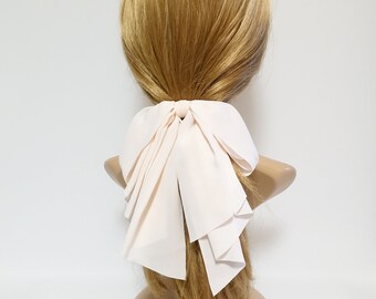 May include: A pale pink fabric hair bow with a large, layered bow. The bow is tied around a ponytail.
