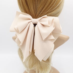 May include: A large, pale pink bow made of soft fabric. The bow is tied with a simple knot and has a layered, ruffled design.