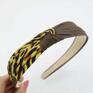 May include: A brown and yellow knotted headband with a leopard print pattern. The headband is made of fabric and has a brown elastic band.