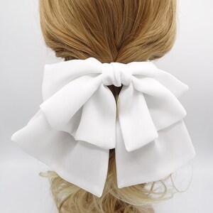 May include: A large white bow hair clip. The bow is made of soft fabric and has a layered design.