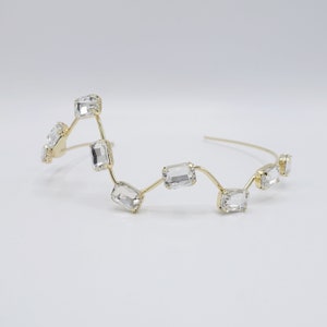 May include: A gold headband with clear rectangular crystals arranged in a wavy pattern.