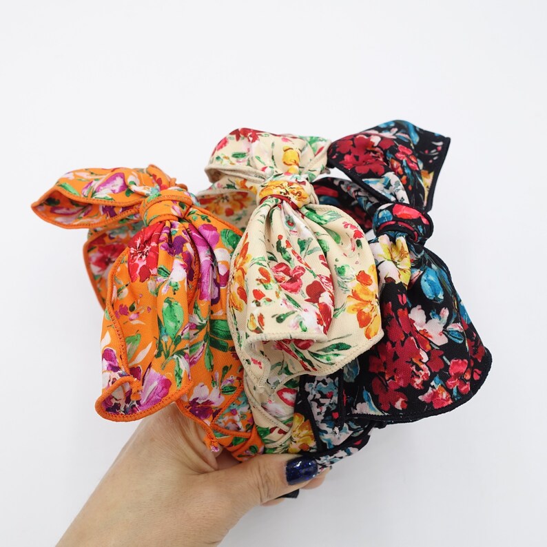 May include: A set of three floral print headbands with bows. The headbands are made of fabric and have a variety of colors, including orange, black, white, and pink.