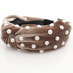 May include: A brown velvet headband with a knotted design and white pearl embellishments.