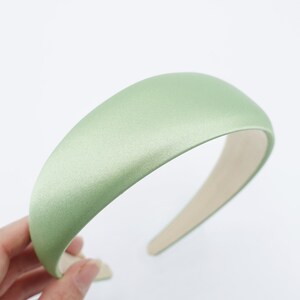 May include: A light green satin headband with a padded, rounded top. The headband is a solid color and has a smooth texture. The interior is a light beige color. The headband is a hair accessory.
