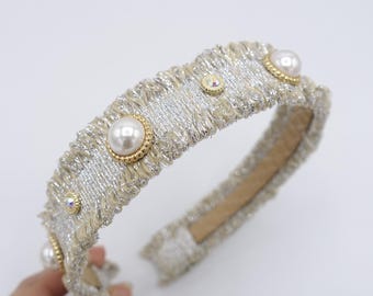 Puede incluir: Una diadema plateada y dorada con perlas de imitación y pedrería. La diadema tiene un diseño texturizado y con flecos con un brillo metálico. Las perlas están engastadas en biseles dorados y la pedrería añade brillo.