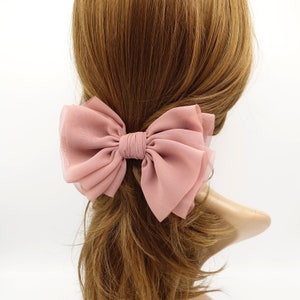 Puede incluir: Un gran lazo rosa para el pelo hecho de tela de gasa. El lazo está atado con un nudo en el centro y tiene un aspecto en capas y con volantes.