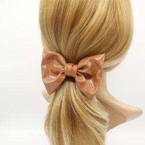 Puede incluir: Una pinza para el pelo de color marrón hecha de cuero sintético en forma de lazo. El lazo está atado en una forma grande y clásica.