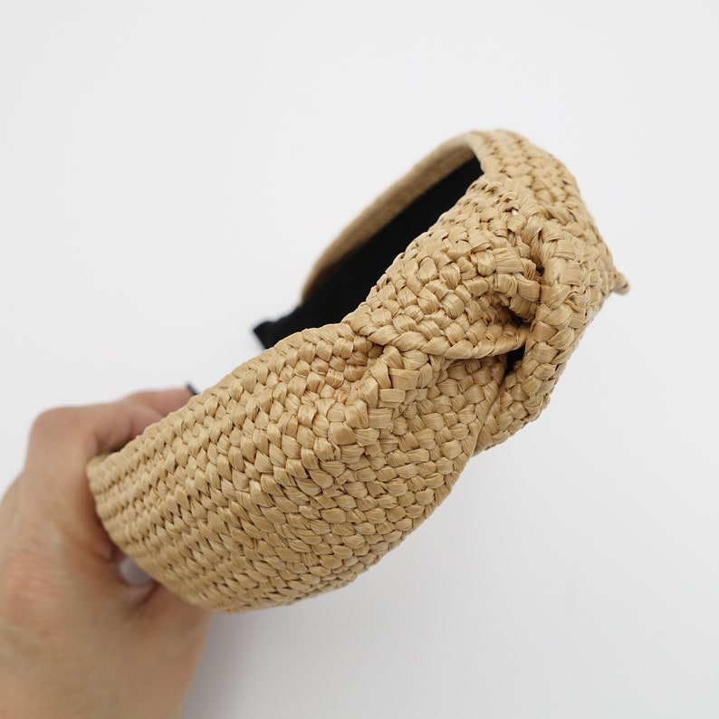 K&ouml;nnte beinhalten: Ein gekn&uuml;pftes Stirnband aus geflochtenem Stroh in hellbrauner Farbe. Das Stirnband ist breit und hat ein schlichtes Design.
