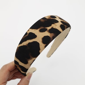 Puede incluir: Una diadema acolchada con estampado de leopardo. La diadema presenta un fondo beige con manchas marrones oscuras. El interior de la diadema es de color beige claro. Un accesorio de moda para la cabeza.