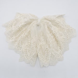 May include: A white lace bow with a delicate floral pattern. The lace is soft and flowing, and the bow is tied in a simple knot.