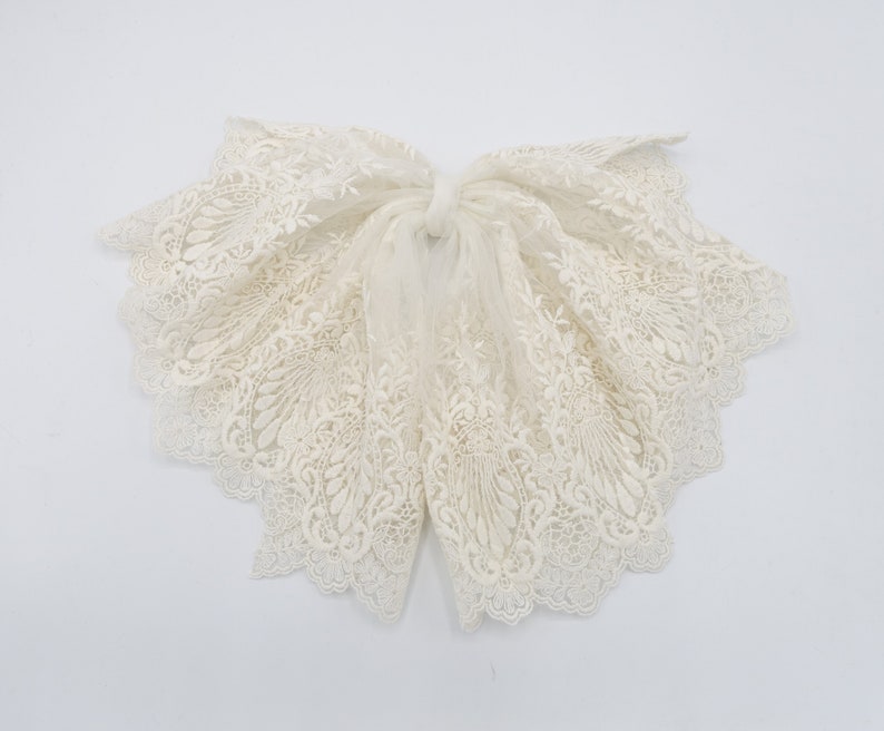 May include: A white lace bow with a delicate floral pattern. The lace is soft and flowing, and the bow is tied in a simple knot.