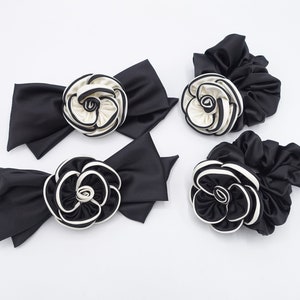 May include: Four black satin hair scrunchies with white and black fabric flower accents.