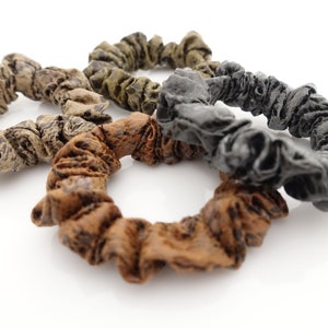 May include: Four scrunchies in different colours and patterns. Two are brown with a black pattern, one is olive green, and one is black.