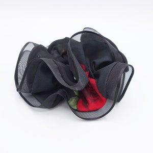 May include: Black hair scrunchie with a red rose print. The scrunchie is made of a soft, stretchy fabric and has a ruffled design.
