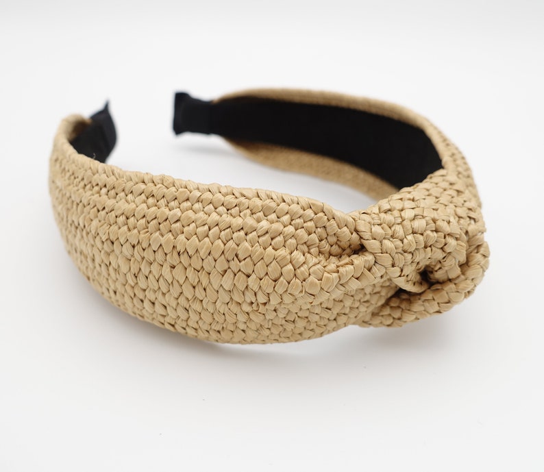 K&ouml;nnte beinhalten: Ein gekn&uuml;pftes Stirnband aus geflochtenem Stroh mit einem schwarzen Gummiband. Das Stirnband ist hellbraun.