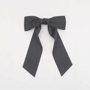 Könnte beinhalten: Eine große schwarze Schleife aus Satin mit langen Bändern. Die Schleife ist in der Mitte verknotet und die Bänder fallen nach unten.