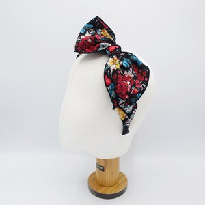 May include: A black headband with a large floral bow. The bow is made of a black fabric with a red, blue, and yellow floral print.