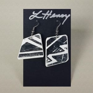 May include: A pair of white ceramic earrings with a black geometric design. The earrings are hanging from silver hooks.