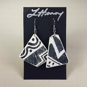 May include: A pair of black and white geometric patterned earrings on a black display card with the word "L'Harmony" written in silver lettering.