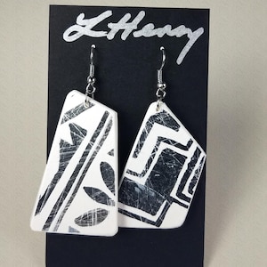 May include: A pair of white ceramic earrings with black geometric designs. The earrings are dangle style with silver hooks.