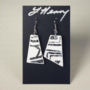 May include: A pair of white geometric earrings with a black and white pattern. The earrings are displayed on a black card with the word "YHenry" written in silver.