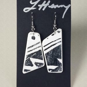 May include: A pair of white ceramic earrings with black geometric designs. The earrings are hanging from silver hooks.